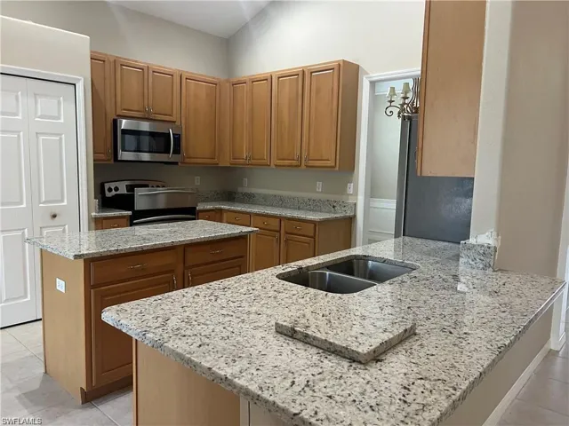 Kitchen with light tile patterned floors, light stone counters, stainless steel appliances, a peninsula, and brown cabinetry