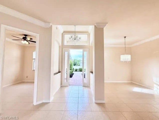 Foyer entrance and dining room with a chandelier, ornamental molding, ceiling fan, and light tile patterned flooring