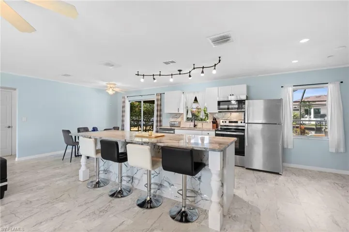 Kitchen with appliances with stainless steel finishes, light stone countertops, a kitchen island, white cabinets, and a breakfast bar