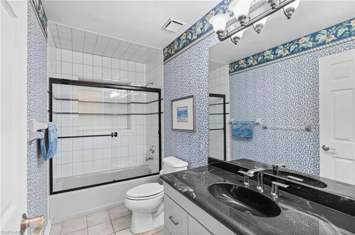 Full bath with combined bath / shower with glass door, light tile patterned floors, vanity, and wallpapered walls