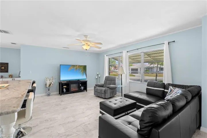 Living area with light marble finish floors, crown molding, and ceiling fan