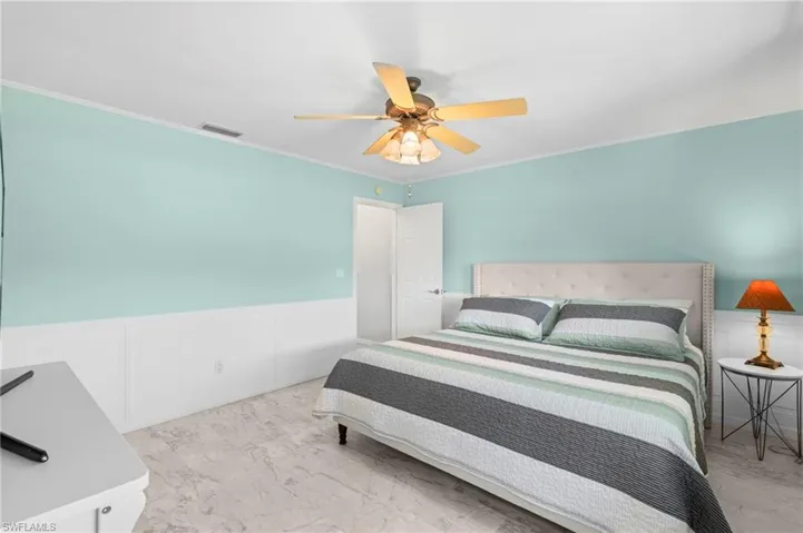 Bedroom featuring wainscoting, a decorative wall, crown molding, and ceiling fan