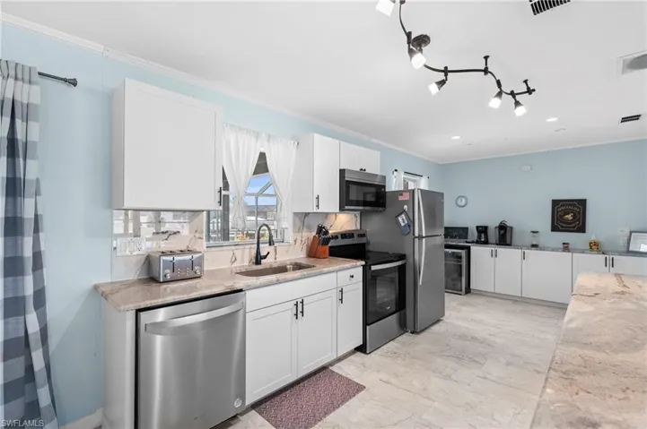 Kitchen with white cabinets, appliances with stainless steel finishes, light stone counters, ornamental molding, and wine cooler