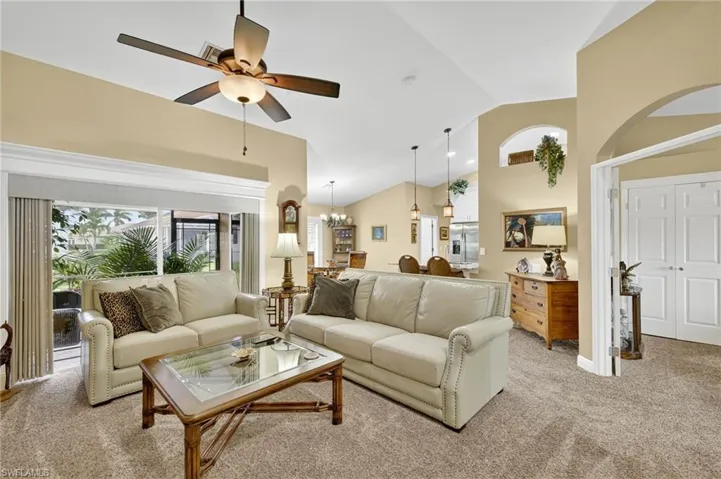 Living room featuring light colored carpet, a ceiling fan, high vaulted ceiling, and a chandelier