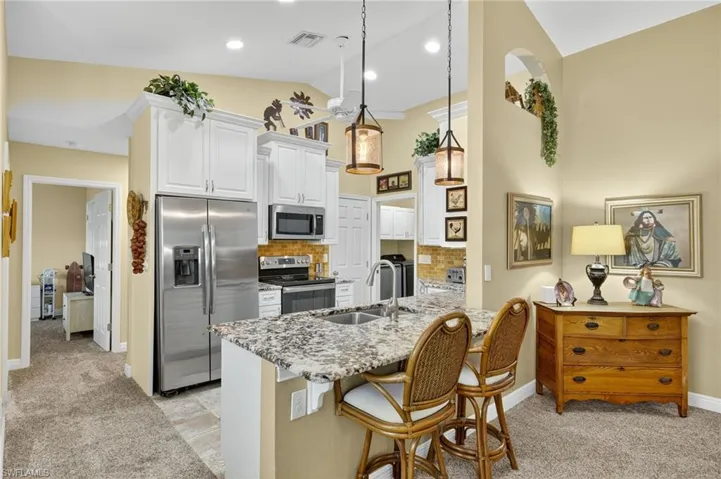 Kitchen featuring tasteful backsplash, appliances with stainless steel finishes, lofted ceiling, white cabinetry, and a kitchen breakfast bar