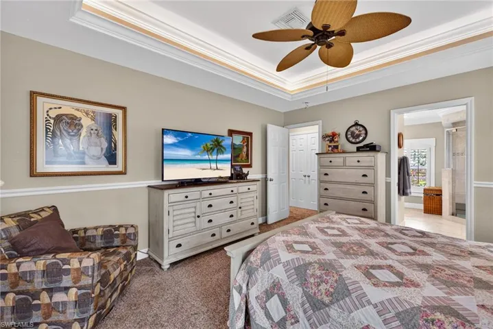 Bedroom with crown molding, a tray ceiling, light colored carpet, a ceiling fan, and ensuite bath