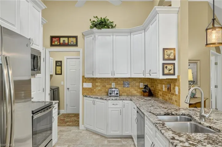 Kitchen featuring white cabinetry, appliances with stainless steel finishes, light stone counters, and decorative backsplash