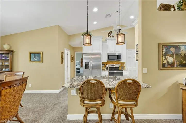 Kitchen featuring light carpet, stainless steel appliances, tasteful backsplash, white cabinetry, and high vaulted ceiling