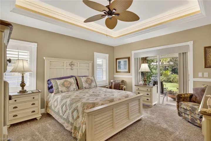Bedroom featuring a tray ceiling, light carpet, ornamental molding, access to outside, and ceiling fan