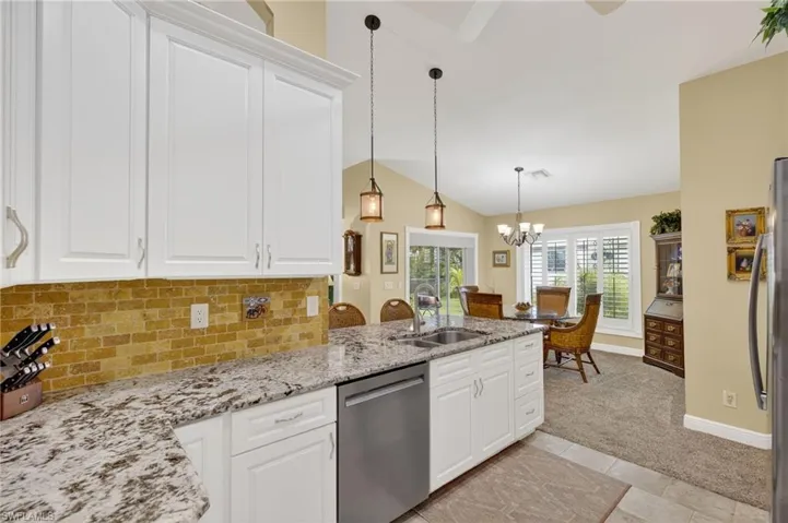 Kitchen with white cabinetry, backsplash, light stone counters, stainless steel appliances, and pendant lighting
