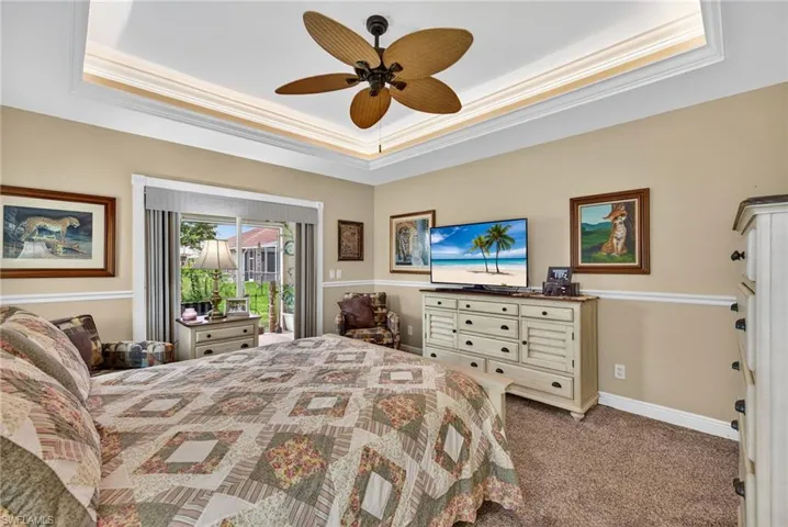 Bedroom featuring a raised ceiling, crown molding, dark carpet, access to exterior, and a ceiling fan