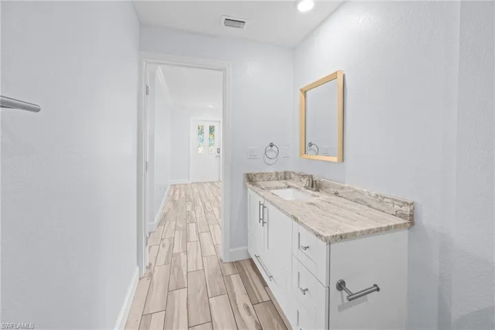 Bathroom with wood finish floors, a textured wall, vanity, and recessed lighting