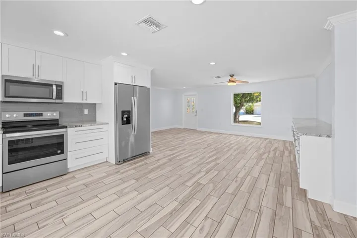 Kitchen with appliances with stainless steel finishes, open floor plan, white cabinets, tasteful backsplash, and recessed lighting