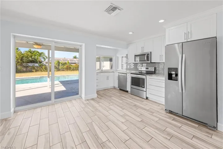 Kitchen featuring stainless steel appliances, white cabinets, backsplash, wood tiled floors, and ornamental molding