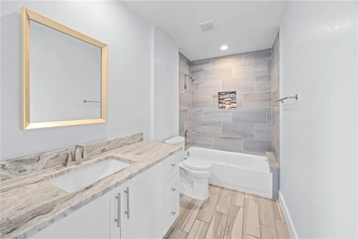 Bathroom featuring vanity, washtub / shower combination, wood finish floors, a textured wall, and recessed lighting