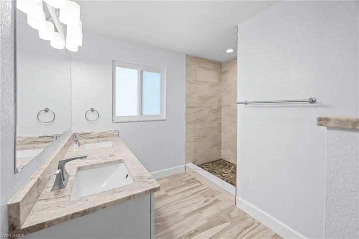 Full bath featuring double vanity, light wood finished floors, a walk in shower, a chandelier, and recessed lighting