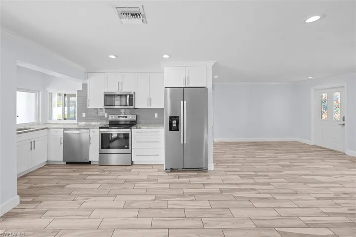 Kitchen featuring crown molding, appliances with stainless steel finishes, white cabinets, decorative backsplash, and wood finish floors