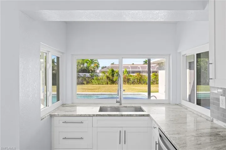 Kitchen featuring white cabinets, light stone countertops, healthy amount of natural light, a textured wall, and dishwasher