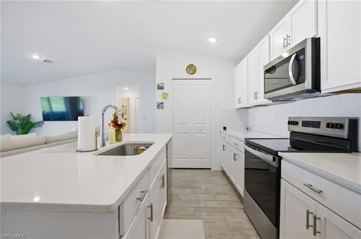 Kitchen featuring appliances with stainless steel finishes, vaulted ceiling, white cabinets, light stone countertops, and open floor plan