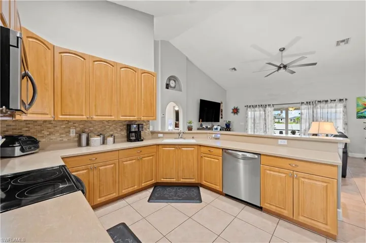 Kitchen featuring stainless steel appliances, high vaulted ceiling, light tile patterned flooring, and kitchen peninsula