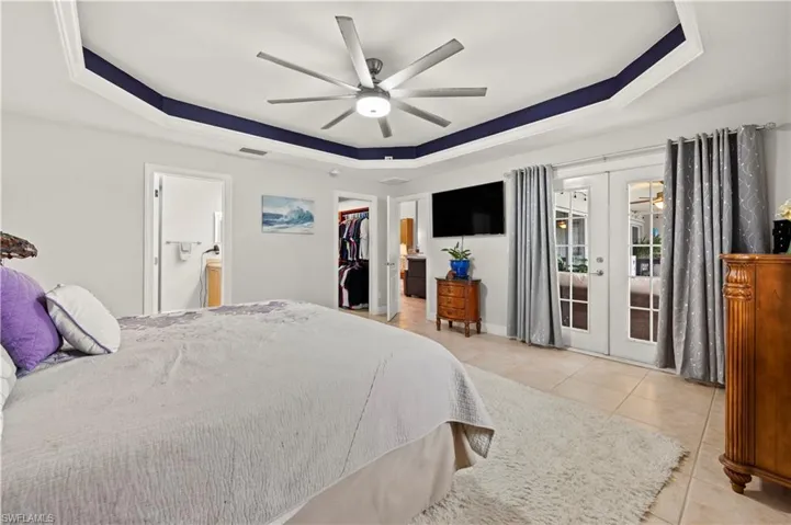 Bedroom featuring a raised ceiling, tile patterned floors, ceiling fan, french doors, and access to outside