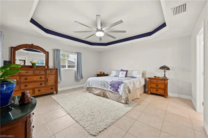 Tiled bedroom with ceiling fan and a tray ceiling