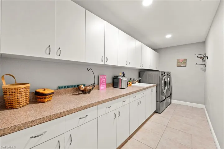 Clothes washing area with sink, washer and clothes dryer, light tile patterned floors, and cabinets