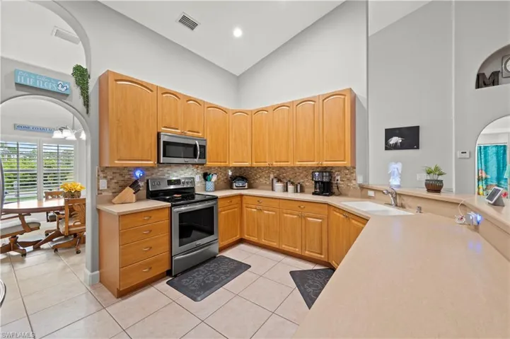 Kitchen featuring appliances with stainless steel finishes, a notable chandelier, high vaulted ceiling, sink, and light tile patterned flooring
