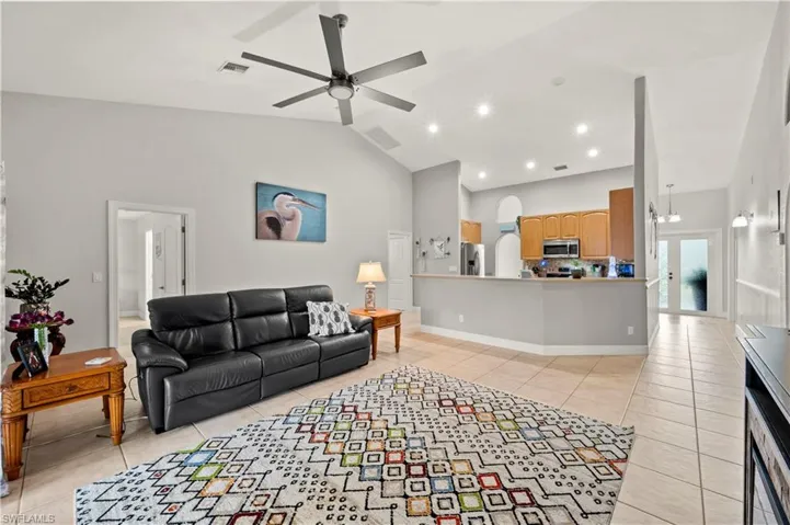 Tiled living room featuring ceiling fan with notable chandelier and high vaulted ceiling