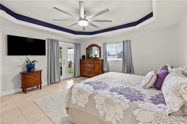 Bedroom with access to outside, french doors, a raised ceiling, ceiling fan, and light tile patterned floors