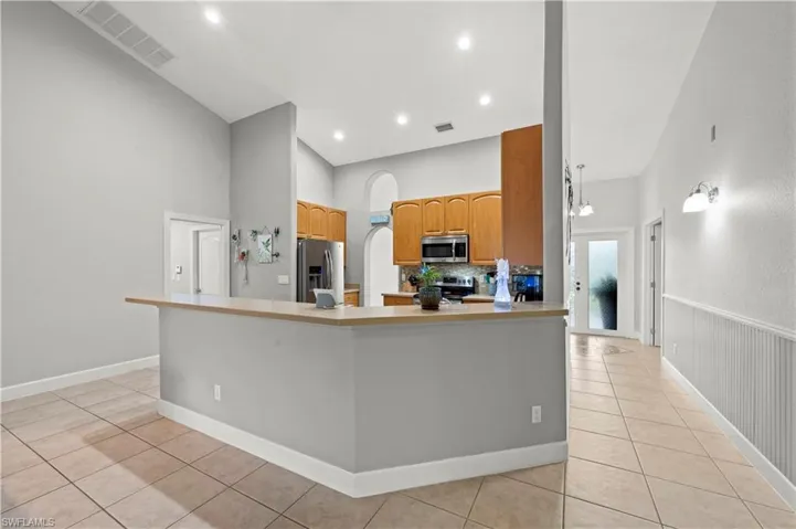 Kitchen with a towering ceiling, kitchen peninsula, appliances with stainless steel finishes, and light tile patterned floors
