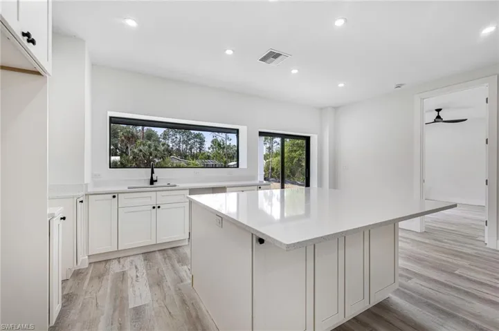 Kitchen with light countertops, visible vents, recessed lighting, a kitchen island, and a sink