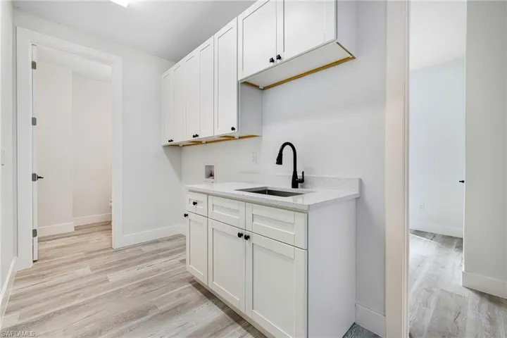 Kitchen with white cabinets, a sink, baseboards, and light wood-type flooring