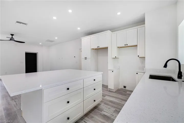 Kitchen with a sink, light stone counters, light wood finished floors, visible vents, and a ceiling fan
