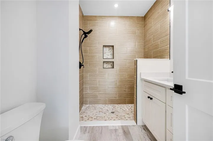 Full bath featuring toilet, wood finished floors, tiled shower, and vanity