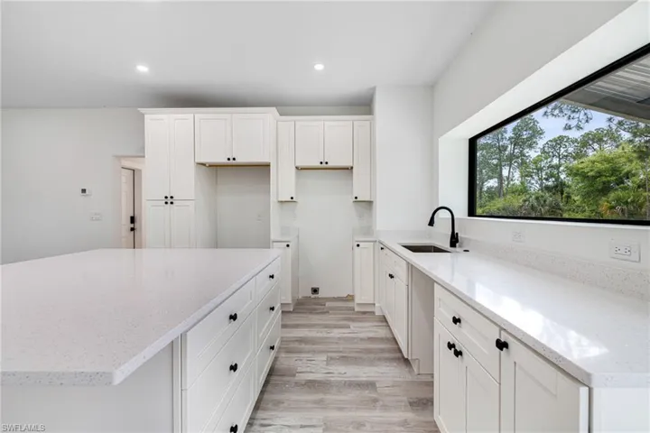 Kitchen with recessed lighting, light wood-type flooring, a sink, light stone counters, and white cabinets