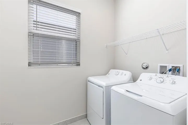 Dedicated laundry space featuring a window with blinds, a wall-mounted wire shelf, and tile flooring