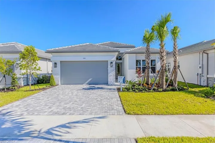 Contemporary exterior with a tiled roof, paver driveway, stone façade accents, and mature palm tree landscaping