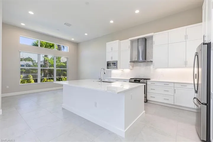 Contemporary kitchen featuring a large central island, white cabinetry, stainless steel appliances, and tile flooring