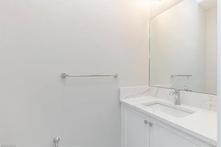 White vanity with integrated sink, stone countertop, chrome faucet, and frameless mirror