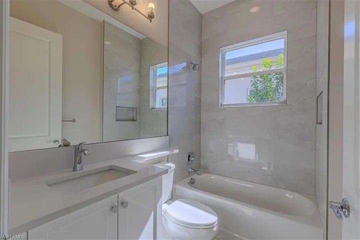 Contemporary bathroom featuring a floating vanity with rectangular vessel sink and quartz countertop, frameless glass shower enclosure with tile surround, soaking tub, and natural light from dual windows