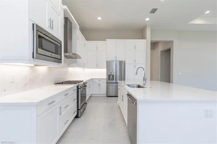 Bright kitchen featuring white cabinetry, light-toned countertops, stainless steel appliances, a kitchen island with an undermount sink, and recessed lighting