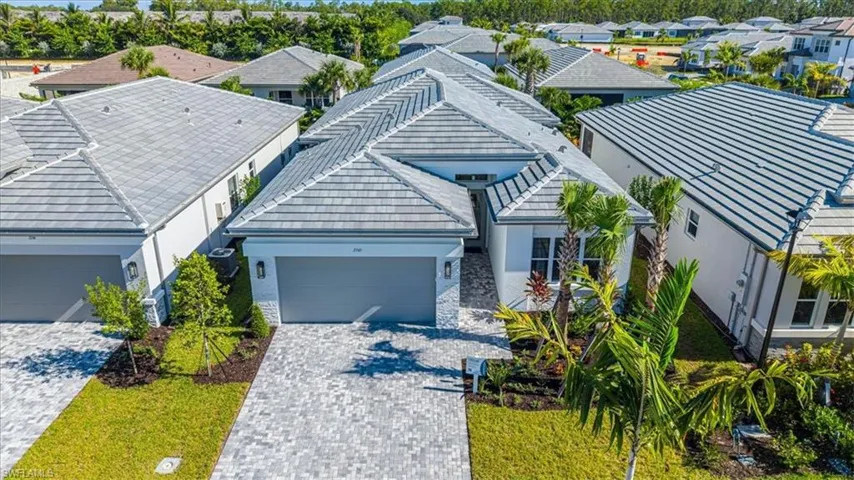 Contemporary exterior design with a tiled roof, paver driveway, attached garage, and tropical landscaping