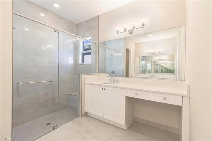 Glass-enclosed shower with a built-in bench, dual vanity with white cabinetry, quartz countertop, and large wall-mounted mirror