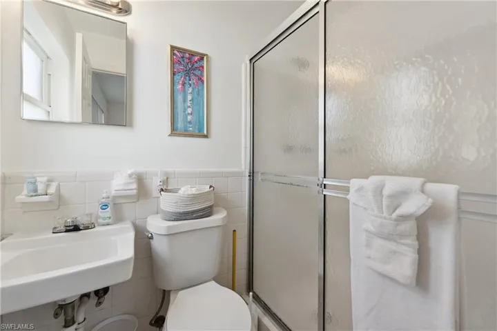 Full bath with toilet, a shower stall, tile walls, a wainscoted wall, and a sink