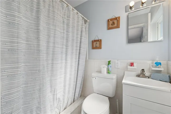 Bathroom featuring vanity, toilet, tile walls, a wainscoted wall, and a shower with curtain