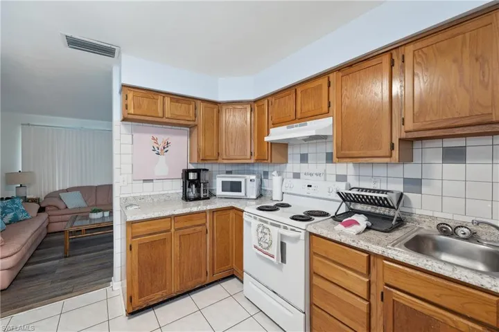 Kitchen with white appliances, under cabinet range hood, a sink, brown cabinets, and light countertops