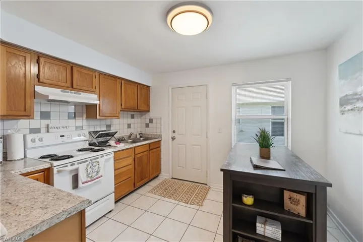 Kitchen with under cabinet range hood, white range with electric cooktop, a sink, backsplash, and light countertops
