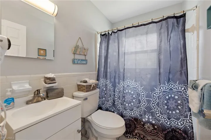 Bathroom with vanity, tile walls, toilet, a shower with curtain, and wainscoting