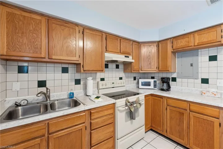Kitchen with white appliances, under cabinet range hood, a sink, electric panel, and light countertops